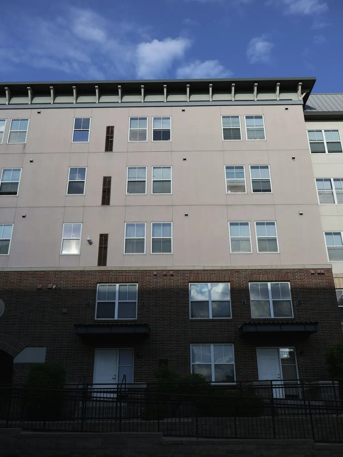 An apartment building with a brick base and light upper storeys under a cloudy sky