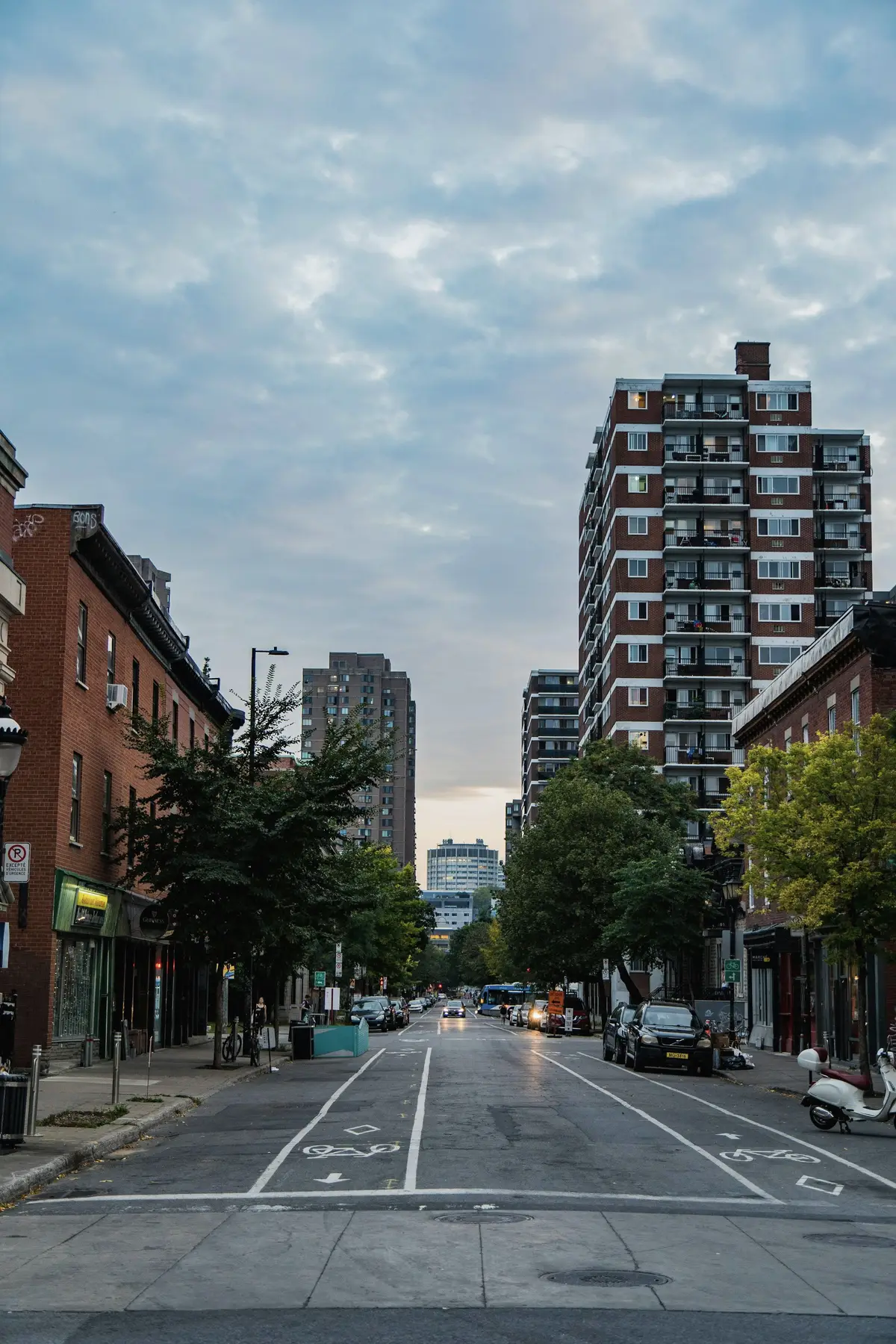 A residential street in Le Plateau-Mont-Royal with parked cars and a tall building beyond