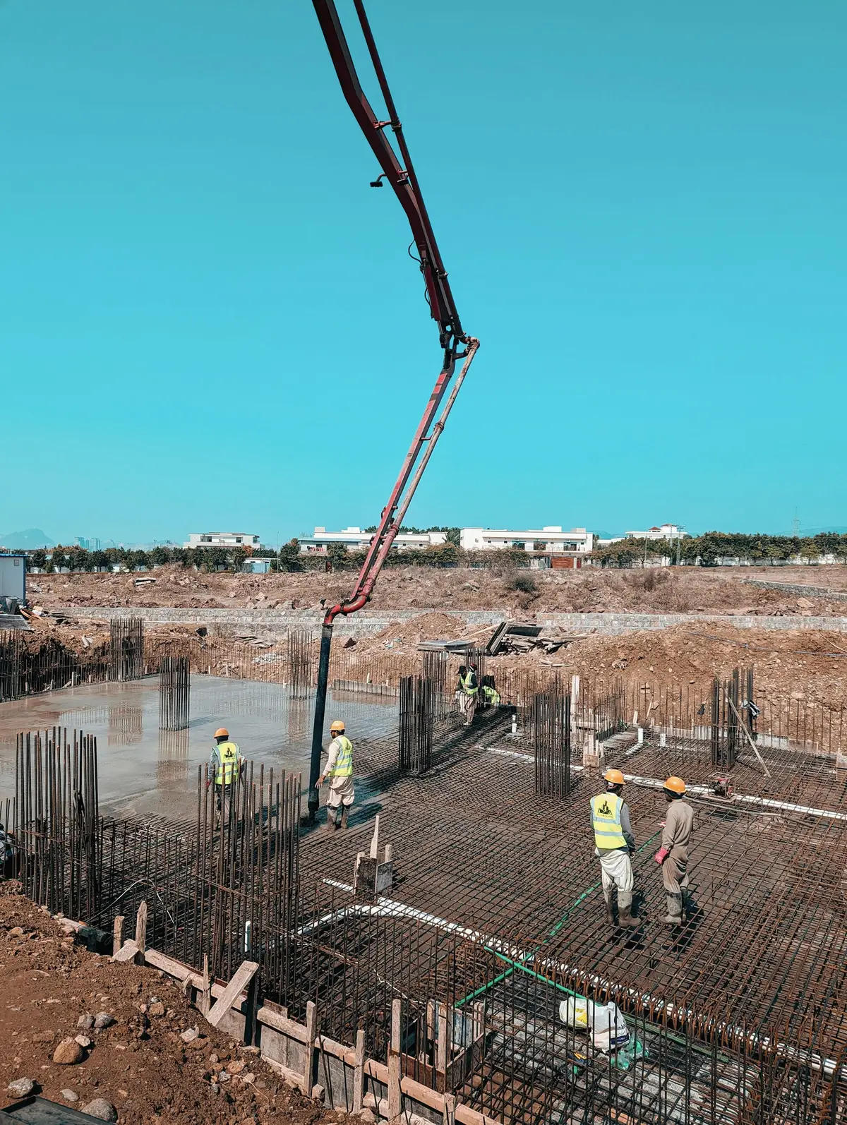 Workers placing reinforcing steel on a concrete slab, with a concrete pump boom above