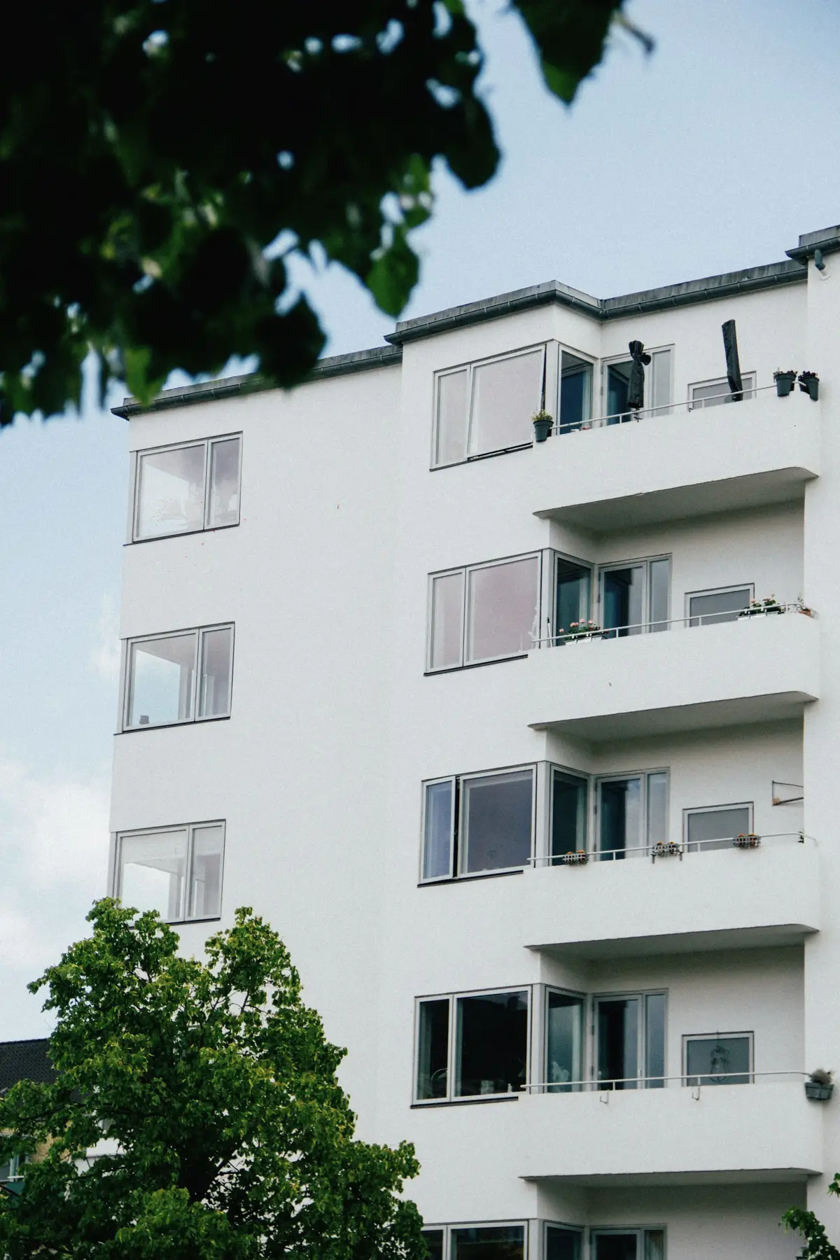 A white apartment building with stacked balconies above trees
